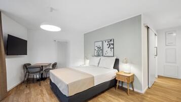 A modern bedroom with a bed, bedside table, lamp, and a desk with a chair.
