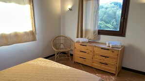 A bedroom with a bed, a wooden dresser, a wicker chair, and a window with curtains.
