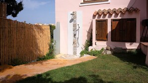 A pink building with a tiled shower area, wooden shutters, and a bamboo fence.