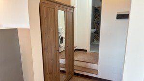 A hallway with a wooden wardrobe, a washing machine, and a bathroom with patterned tiles.
