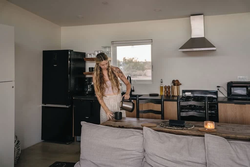 A modern kitchen with a black refrigerator, a coffee machine, and a wooden dining table with a candle.