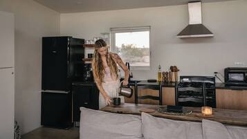 A modern kitchen with a black refrigerator, a coffee machine, and a wooden dining table with a candle.