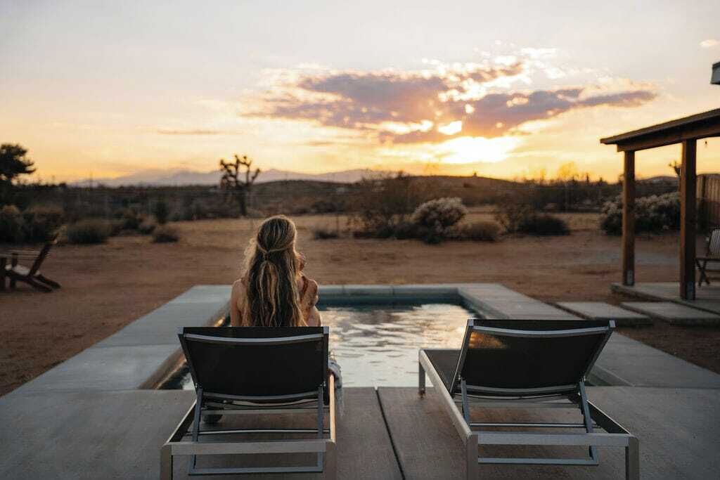 A person sitting on a lounge chair by a pool with a sunset view.