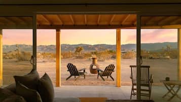 A room with a large glass door leading to an outdoor area with two Adirondack chairs and a table.