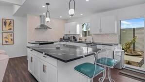Una cocina moderna con una isla central, armarios blancos y un amplio ventanal con vistas a un jardín de cactus.