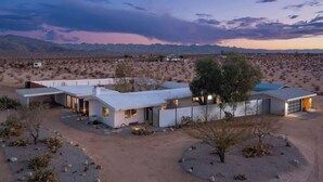 Una casa moderna con techo plano, ventanas amplias y garaje, rodeada por un paisaje desértico.