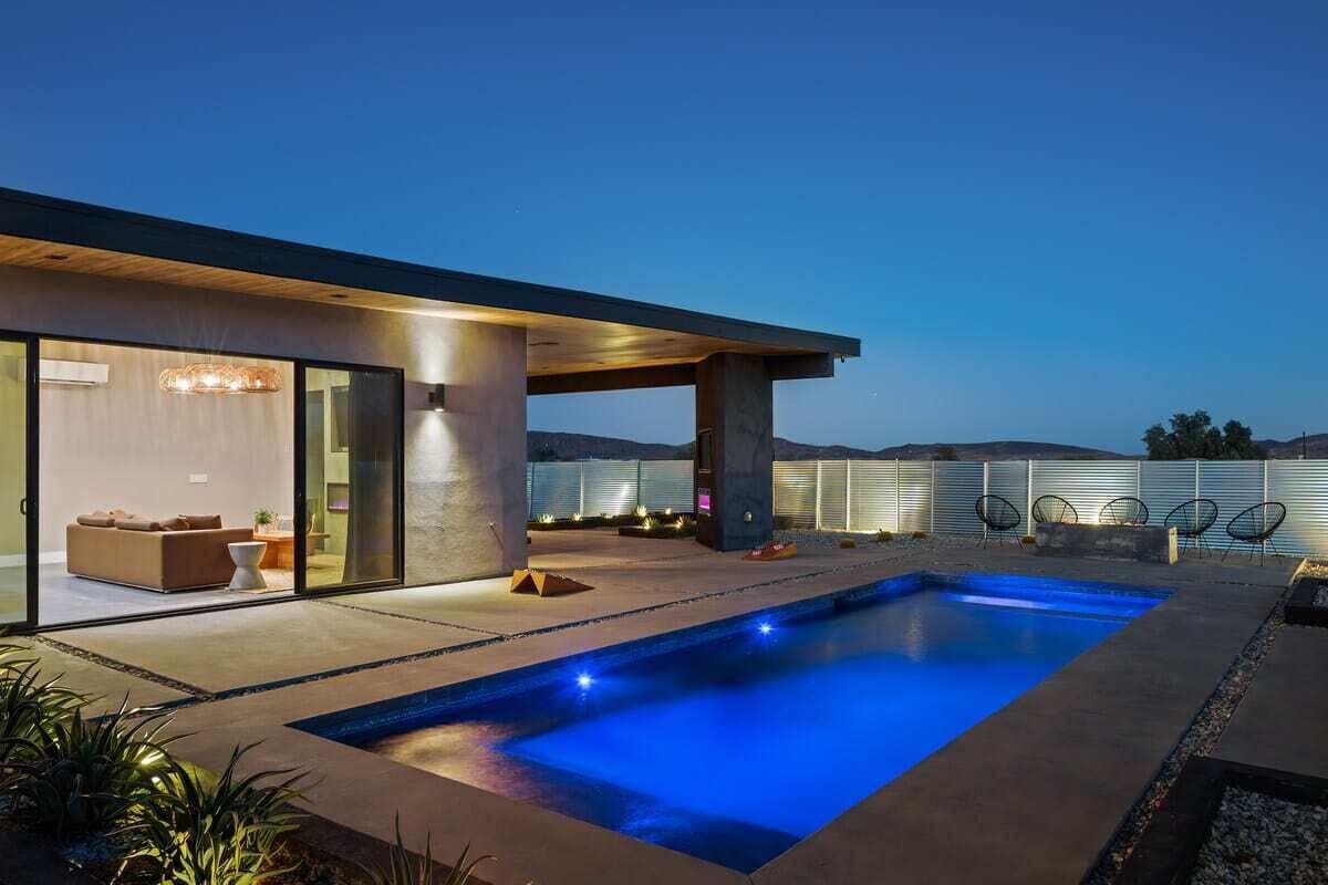 A modern house with a swimming pool, glass doors leading to a living area, and a view of the mountains.
