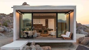 A modern, glass-enclosed building with a dining area, kitchen, and seating space. - Prism • Modern Luxury in Boulders, Pool & Hot Tub (Joshua Tree)