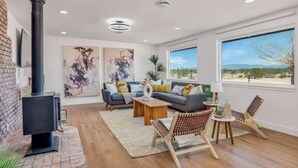 A modern living room with a fireplace, a sofa set, a coffee table, and a view of the outdoors. - Winters Haven · 2.5 Acres, Spa, PingPong, SoakPool (Joshua Tree)