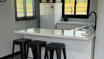 A compact kitchen with a white countertop, black stools, a sink, and a clock on the wall.