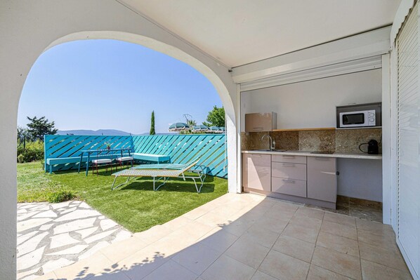 Une terrasse avec vue sur la montagne, un espace extérieur bleu aménagé avec des sièges, et une cuisine équipée d’un four à micro-ondes.