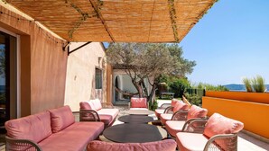 An outdoor seating area with wicker furniture and cushions, a pergola overhead, and a view of the sea and hills in the background. - Splendid Flat in Provencal Villa 1br/3p (Grimaud)
