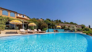A swimming pool with lounge chairs and umbrellas, surrounded by a landscaped garden and a building with arched windows. - Splendid Flat in Provencal Villa 1br/3p (Grimaud)