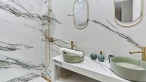 Un baño con pared de mármol, cabezal de ducha dorado, lavamanos verde y espejo con marco dorado.