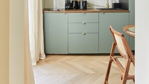 Una cocina compacta con armarios verde claro, un protector contra salpicaduras de mármol y una encimera de madera.