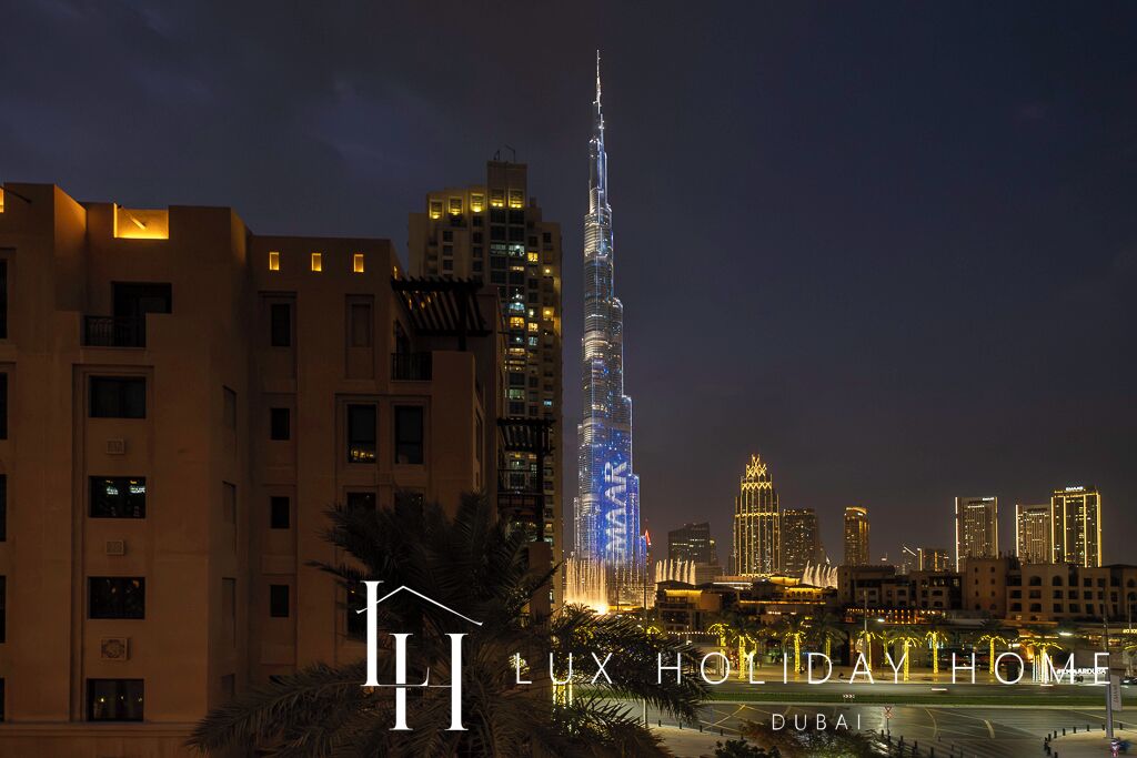 Una vista nocturna de un paisaje urbano con el Burj Khalifa iluminado al fondo, rodeado de otros edificios.