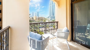 A balcony with a view of Dubai's skyline, white wicker furniture, and a glass door.
