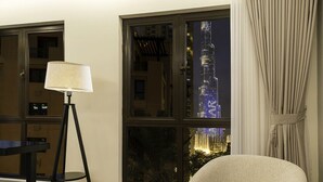 A room with a view of a tall illuminated building at night, a lamp, and a curtain.