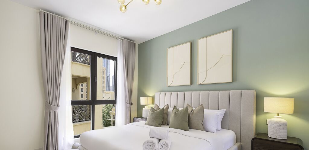 Een hotelkamer met een groot bed, twee nachtkastjes, een raam met gordijnen en twee kunstwerken aan de muur.