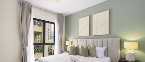 Een hotelkamer met een groot bed, twee nachtkastjes, een raam met gordijnen en twee kunstwerken aan de muur.