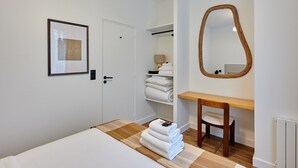 A hotel room with a bed, a wooden bench, a mirror, a framed picture, and a shelf with folded towels. - Charming & Modern Apartment Center of Paris (Paris)