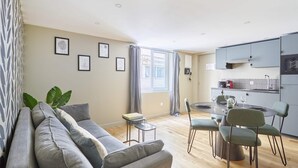 Een moderne woonkamer met een bank, een eettafel, stoelen en een keukenhoek met kasten en een raam.