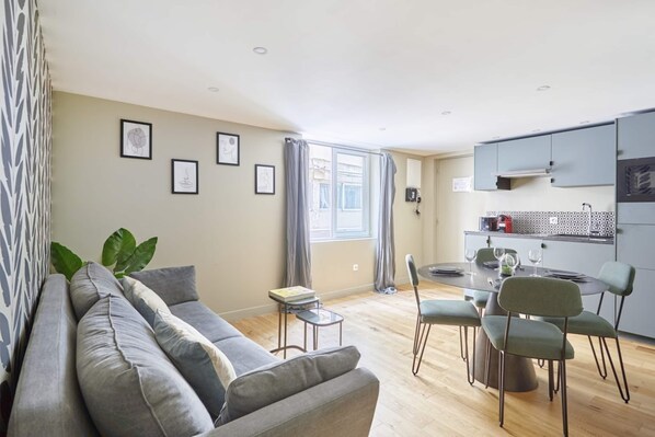 Ein modernes Wohnzimmer mit einer Couch, einem Esstisch, Stühlen und einer Küchenzeile mit Schränken und einem Fenster.