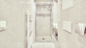 Een moderne badkamer met een douche met glazen wand, een witte handdoekhouder en een handdoekdispenser.