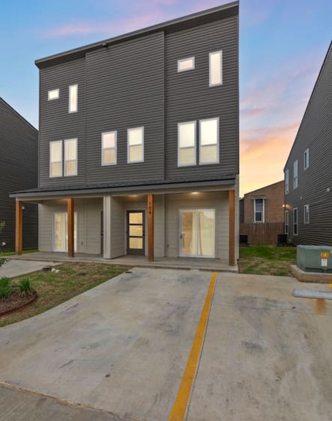 A two-story apartment building with a flat roof, large windows, and a concrete driveway.