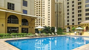 Una piscina con lettini e ombrelloni, circondata da edifici alti.