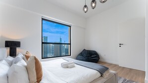 Una camera da letto moderna con una grande finestra, un letto, un pouf e una lampada da comodino.