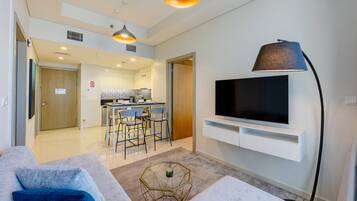 A modern living room with a sofa, a coffee table, a TV mounted on the wall, and a kitchen in the background.