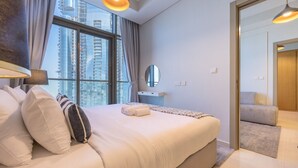 Ein modernes Hotelzimmer mit einem großen Bett, einem Schminktisch mit Spiegel und Blick auf hohe Gebäude durch das Fenster.