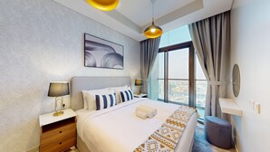 Ein modernes Hotelzimmer mit einem großen Bett, einem Nachttisch mit Lampe, Blick auf die Stadt durch große Fenster und einer Deckenleuchte.