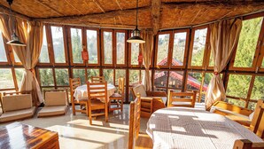 A rustic wooden room with large windows, a round table, and several wooden chairs.
