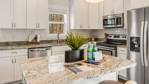 A modern kitchen with white cabinets, a granite countertop, stainless steel appliances, and pendant lighting.