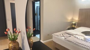 Een slaapkamer met een bed, nachtkastjes, een spiegel en een vaas met bloemen.