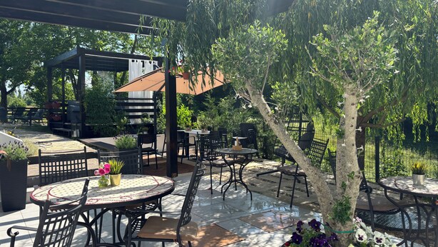 Een terras buiten met ronde tafels en stoelen, een pergola en een barbecueplek.