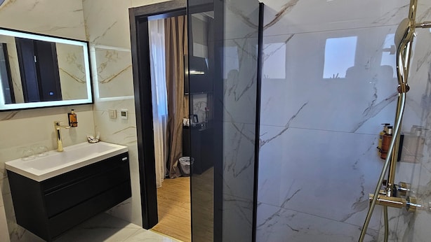 Een moderne badkamer met een douche in een glazen cabine, een wastafel met spiegel en een marmeren vloer.
