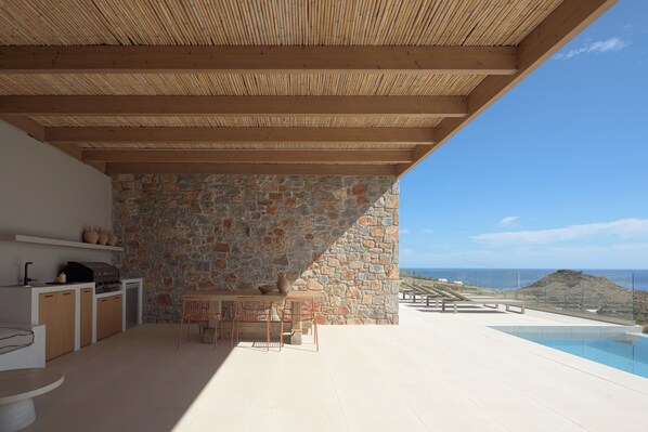 An outdoor patio with a stone wall, wooden ceiling, and a view of the ocean.
