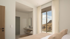 Ein modernes Schlafzimmer mit großem Fenster, einem Bett, einem Nachttisch und einem durchgegangene Tür sichtbaren Badezimmer.
