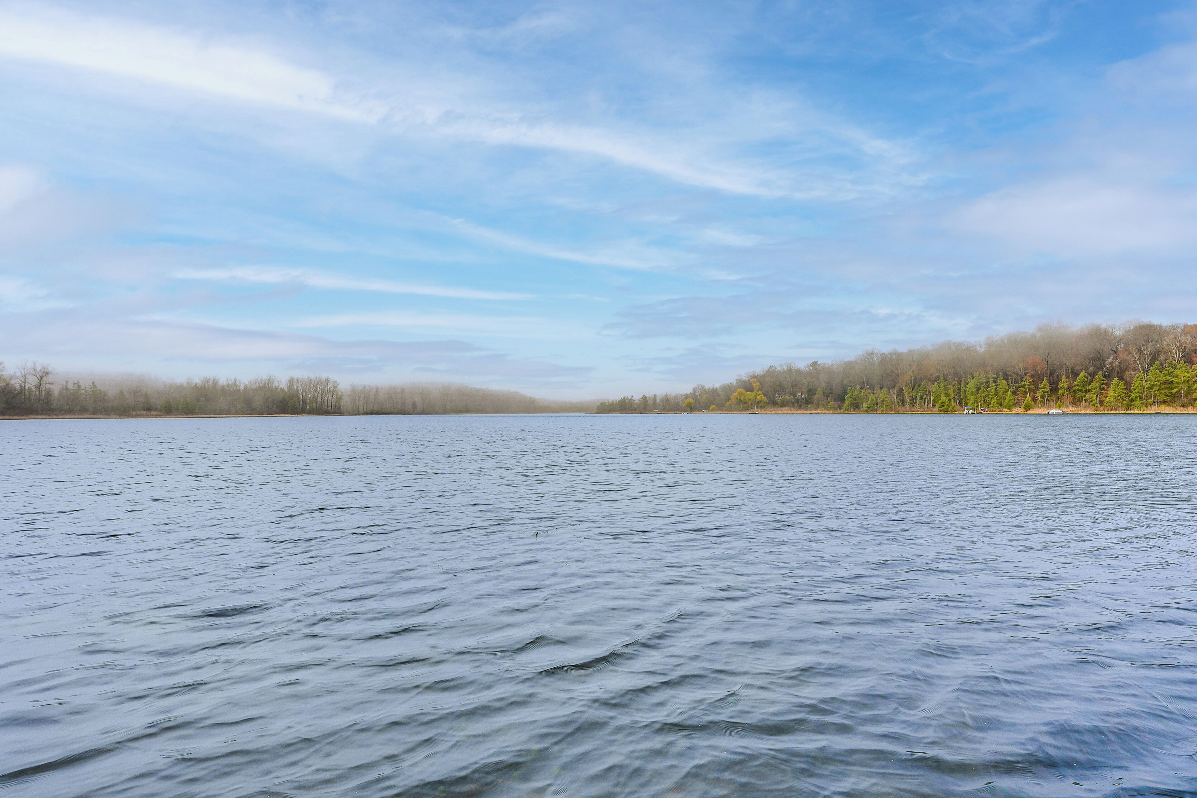 Um lago calmo com margens florestais e céu claro.