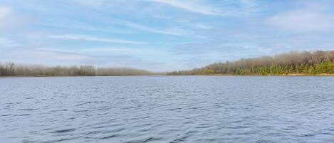 Um lago calmo com margens florestais e céu claro.