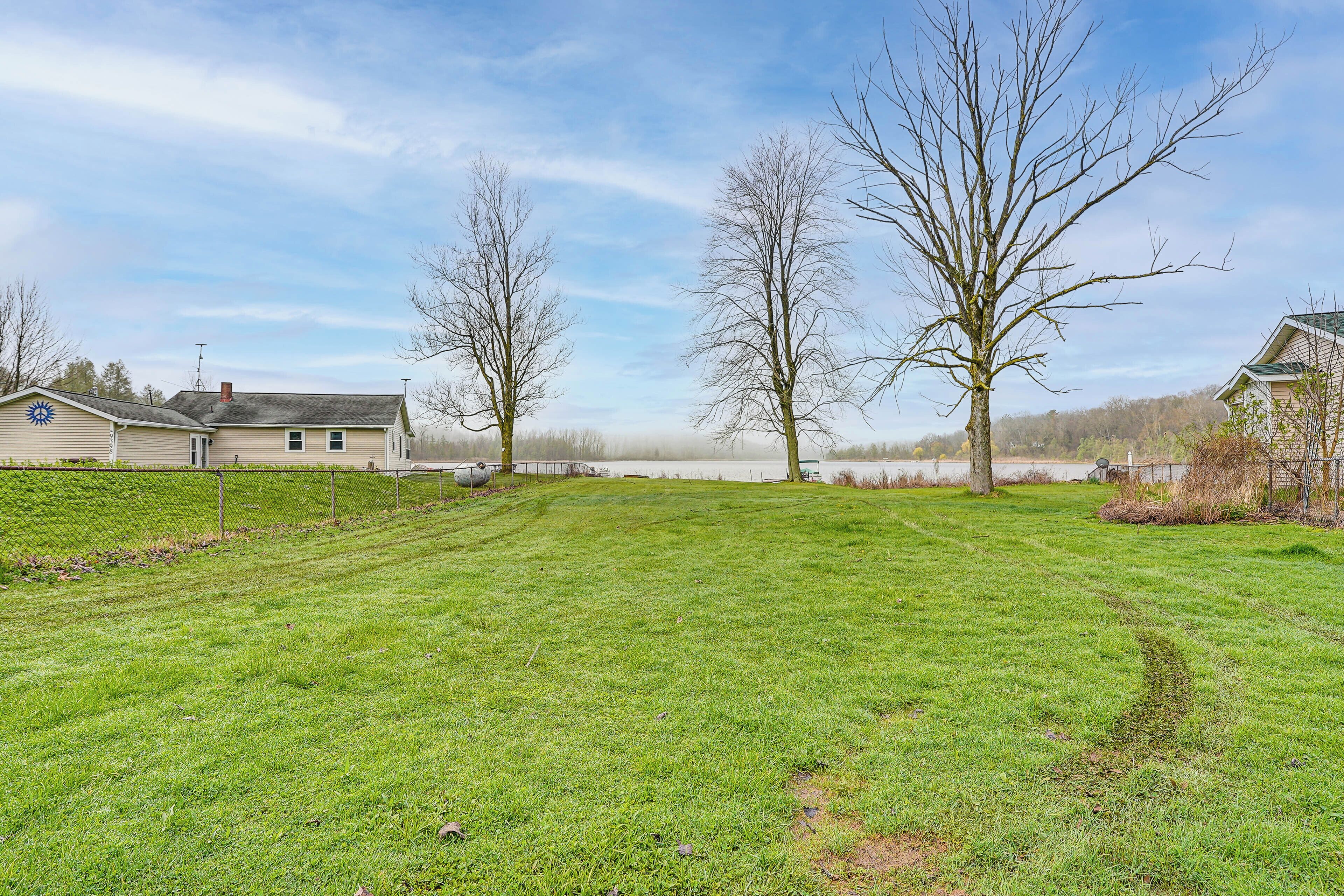 A grassy yard with a house, a large tree, and a lake in the background.