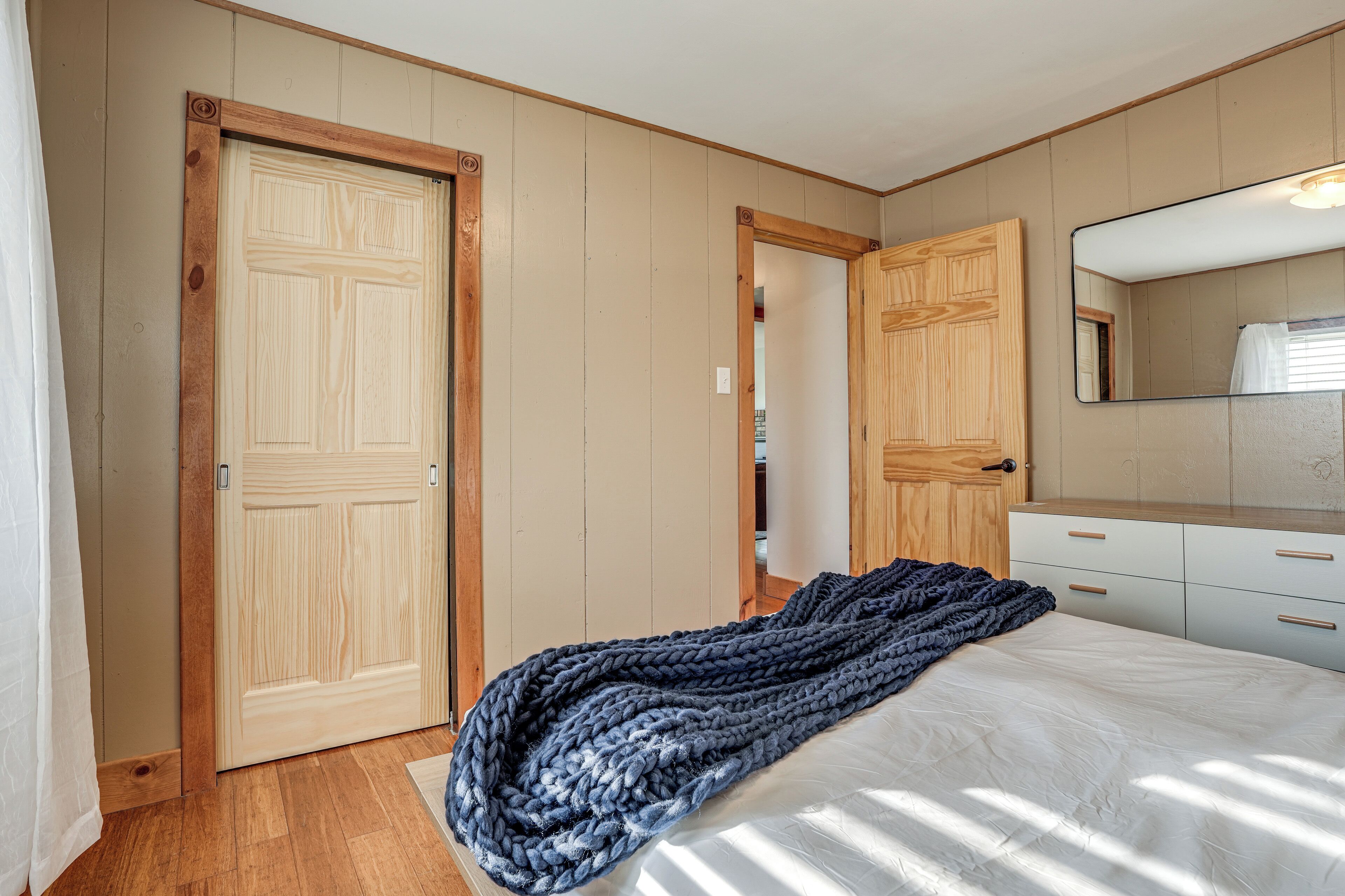 A bedroom with wooden doors, a bed with a white mattress, a large mirror, and a dark blue blanket.