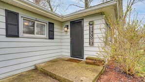 Ein Haus mit dunklem Eingangsbereich, einem Willkommensschild, einem Fenster mit Fensterläden und einer kleinen Veranda.