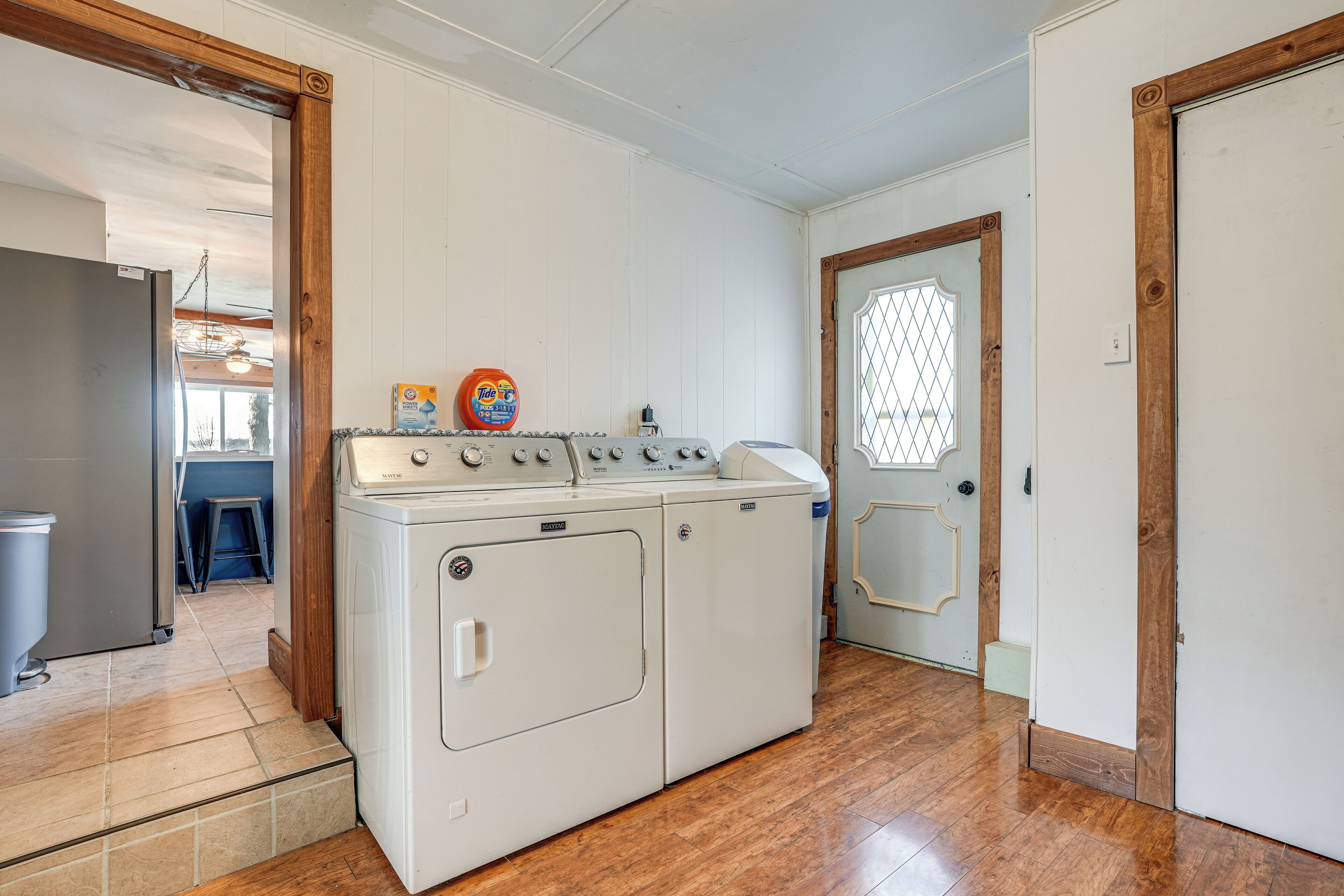 A laundry room with a front-loading washer and dryer, wooden flooring, and a door with a decorative glass panel.