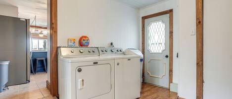 A laundry room with a front-loading washer and dryer, wooden flooring, and a door with a decorative glass panel.