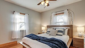Ein Schlafzimmer mit einem hölzernen Bett, weißer Bettwäsche, einer dunkelblauen Decke, zwei Nachttischen mit Lampen und einem Deckenventilator.