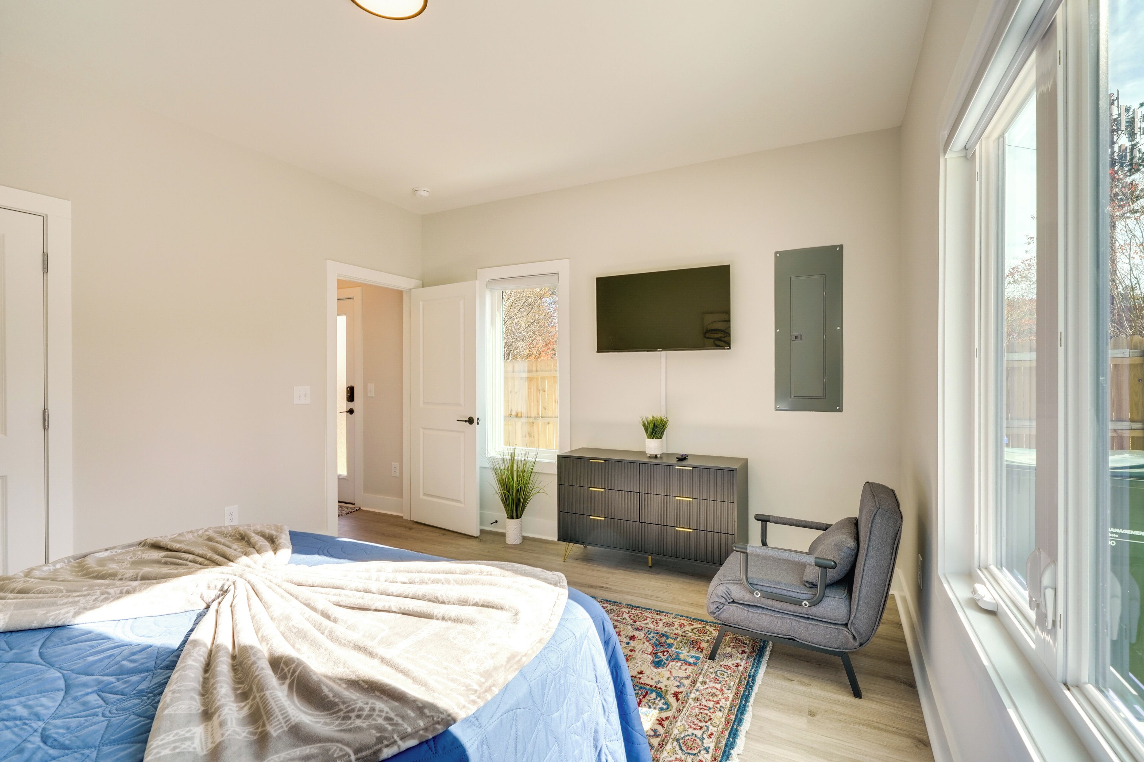 A bedroom with a bed, dresser, chair, and a TV on the wall.
